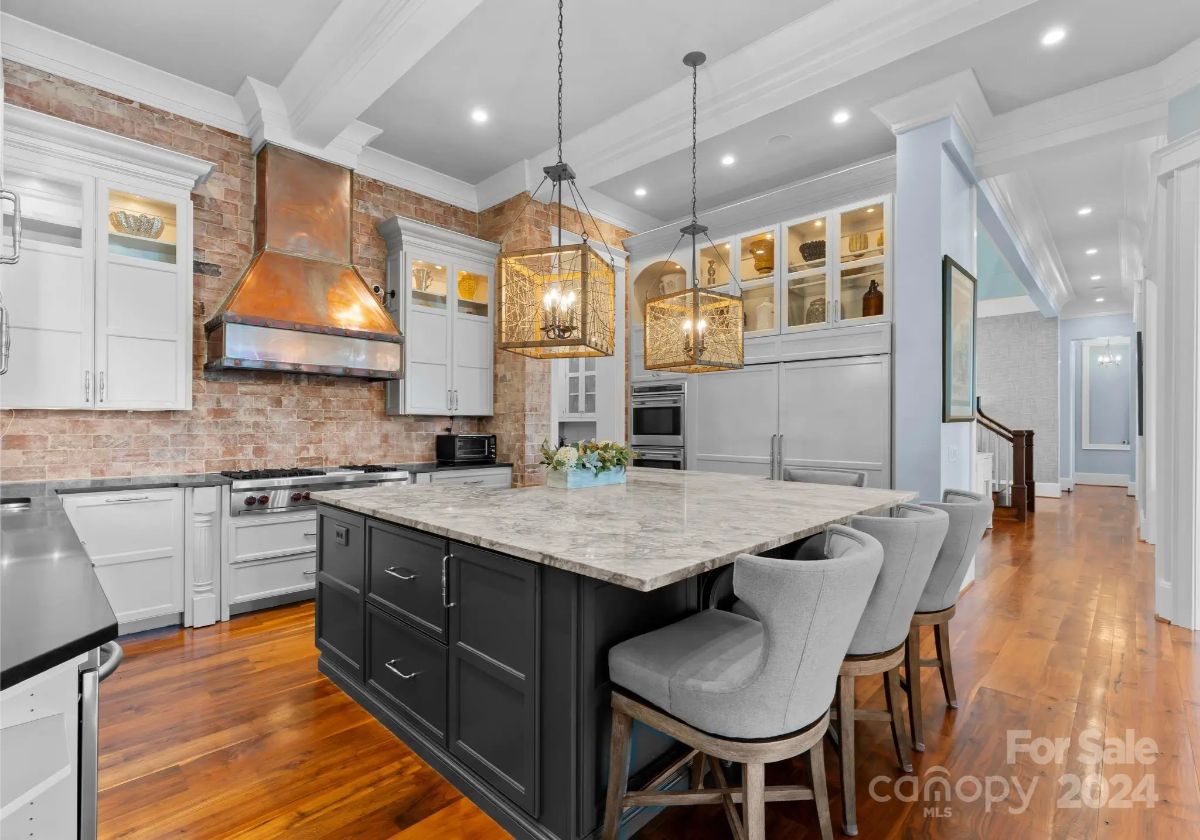 Chef’s kitchen with exposed brick, marble countertops, and lantern-style lighting fixtures. 