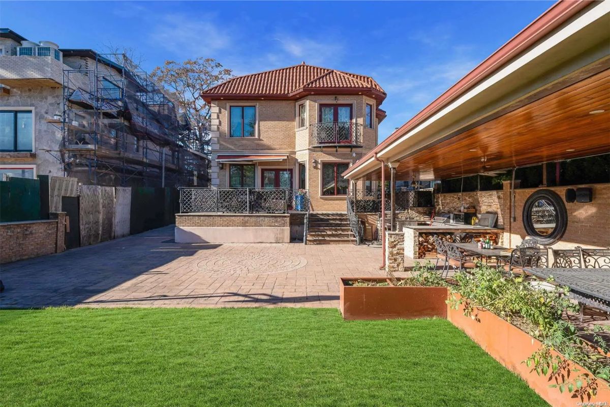 Two-story home with a red tile roof faces a large paved courtyard and green lawn.