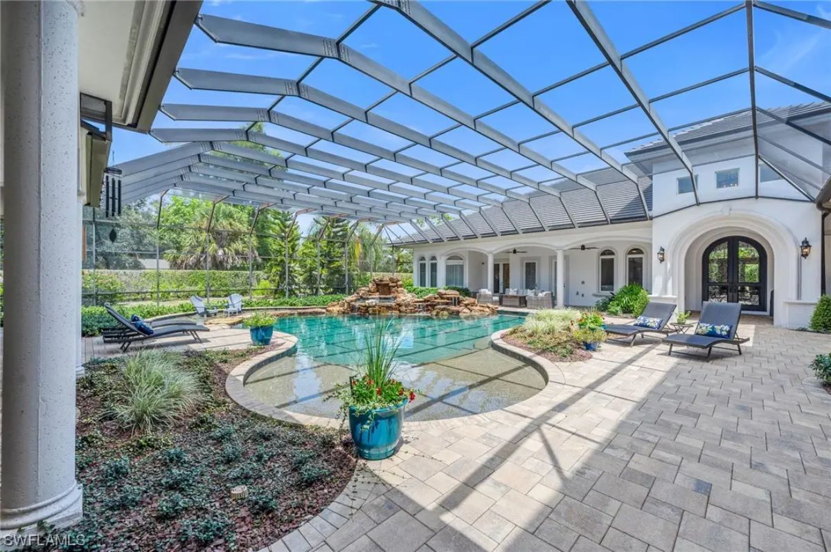 Pool curves around a central rock waterfall under a screened enclosure.
