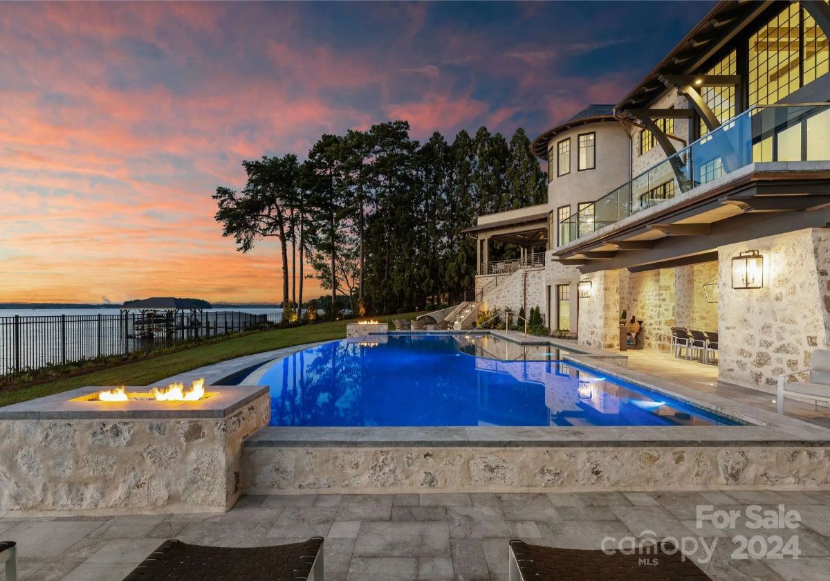 Flames flicker beside a glowing infinity pool as sunset casts the sky in shades of gold and violet. 