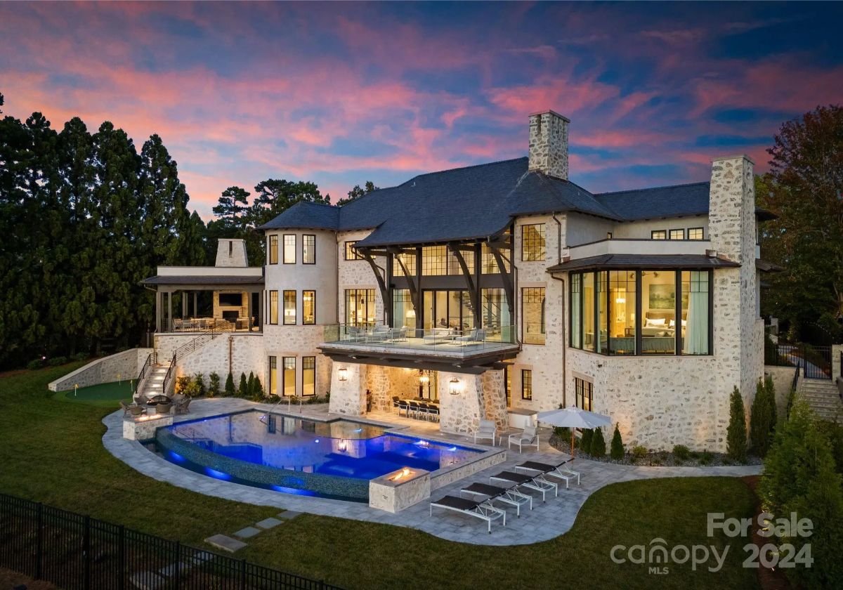 Fiery pink and orange hues paint the sky as a grand lakeside estate glows against twilight. 