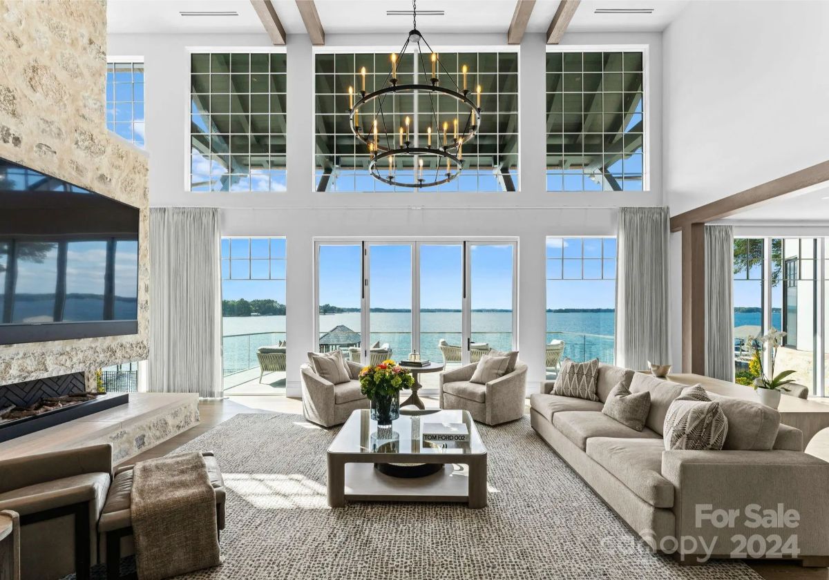 Towering windows flood a living room with golden sunlight, offering breathtaking lake views. 