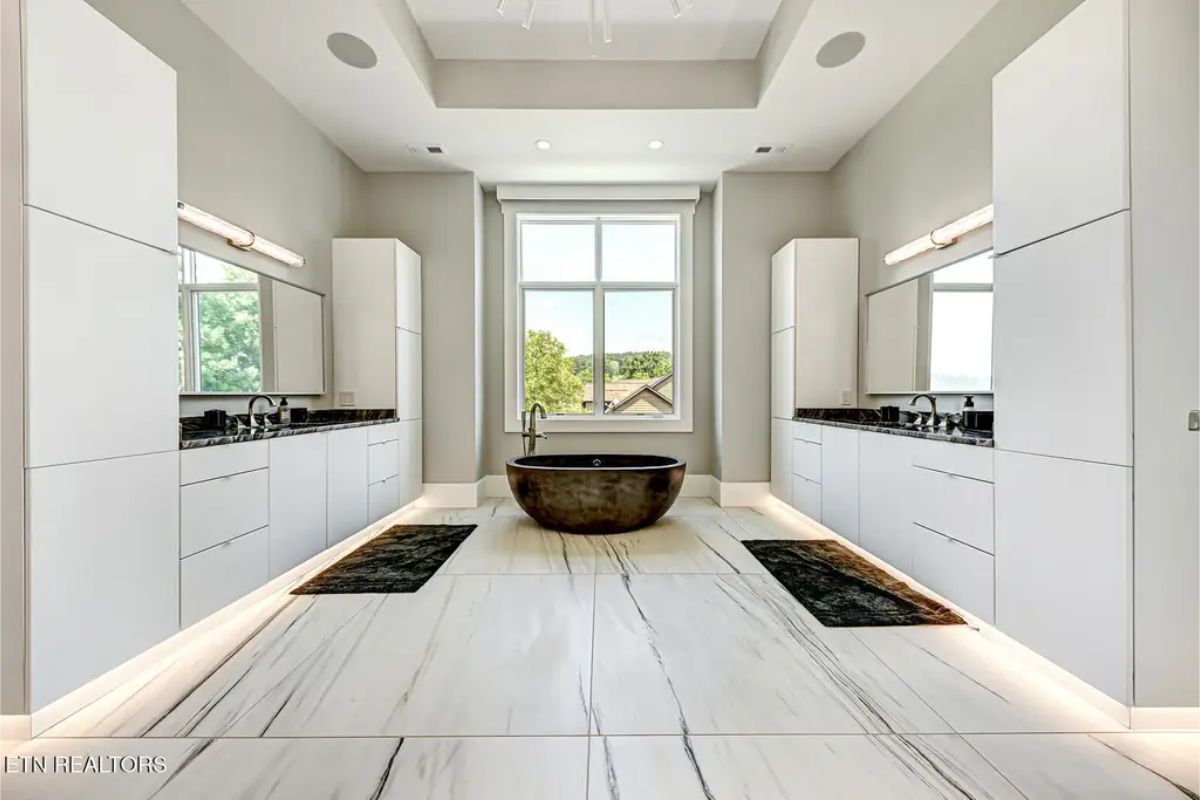 Elegant bathroom with dual vanities, a freestanding stone bathtub, and floor-to-ceiling windows letting in natural light. 