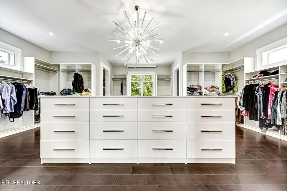 Spacious walk-in closet featuring an island with drawers, open shelving, and a striking modern chandelier. 