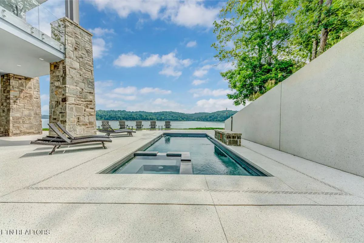 Sleek modern pool area features an elegant rectangular design, built-in spa, and lounge chairs overlooking a scenic lakeside backdrop. 