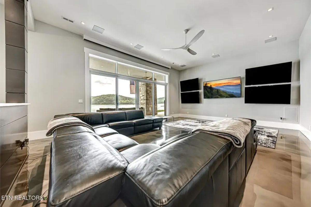 Cozy media room with a large leather sectional, multiple wall-mounted TVs, and an open view to the outdoor patio. 