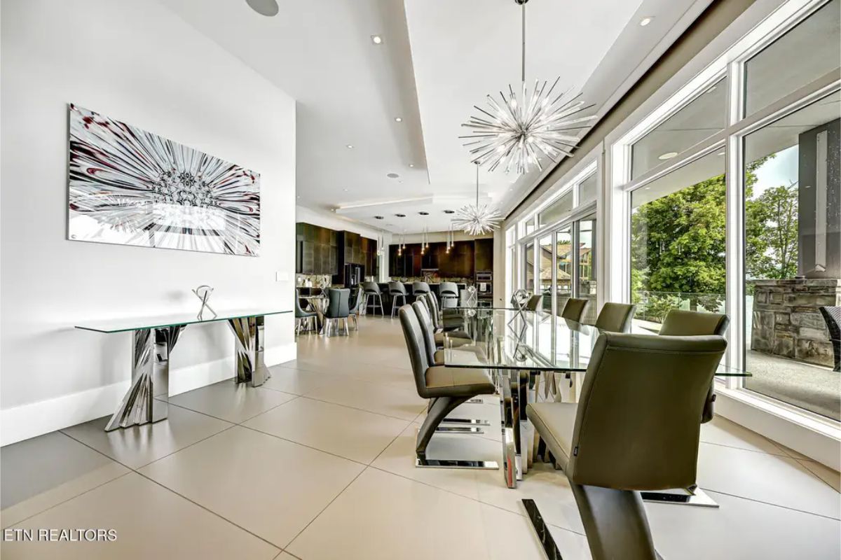 Stylish dining area with floor-to-ceiling windows, modern chandeliers, and a sleek glass table with black leather chairs. 