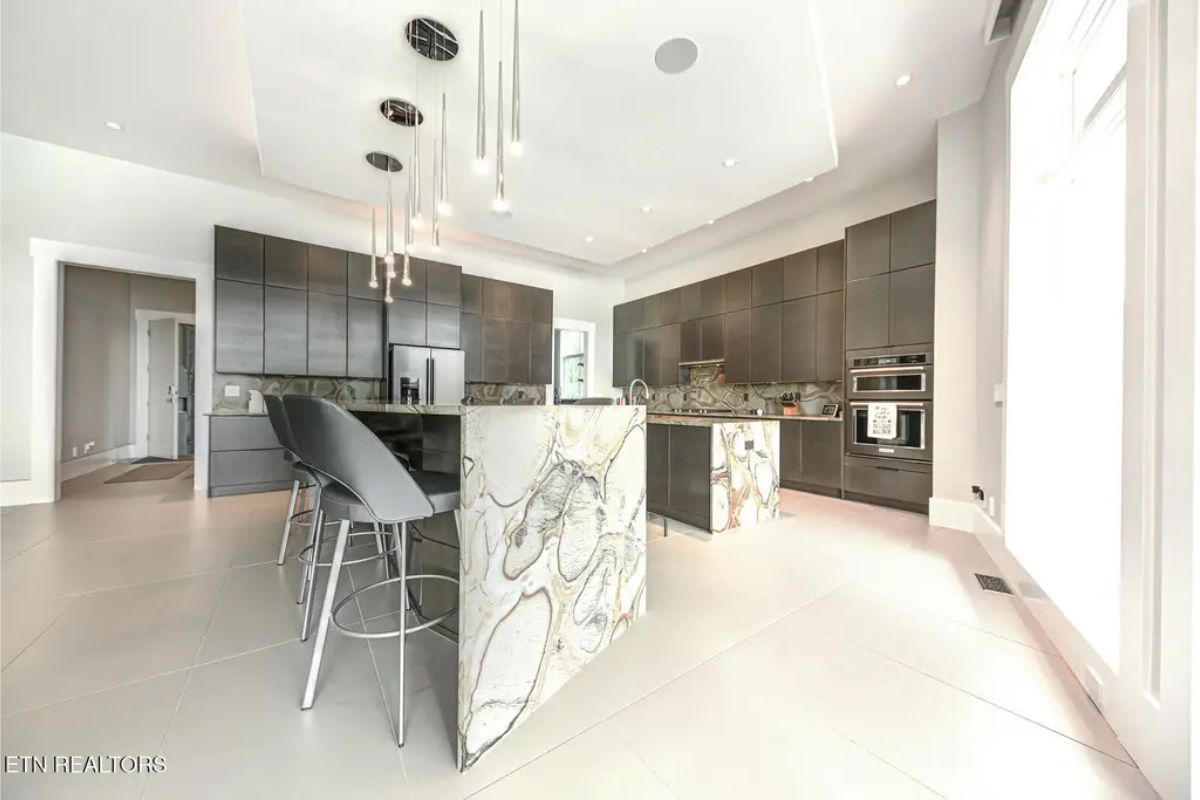 Open-concept kitchen with a bold, marble-accented island, dark cabinetry, and modern lighting fixtures. 