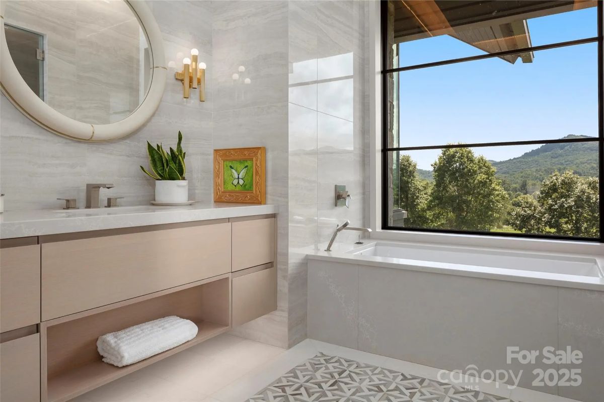 Soft golden light spills across a spa-like bathroom, where a deep soaking tub overlooks rolling hills. 