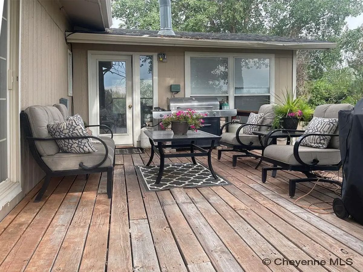 Wooden deck is furnished with cushioned chairs and a glass-top table.