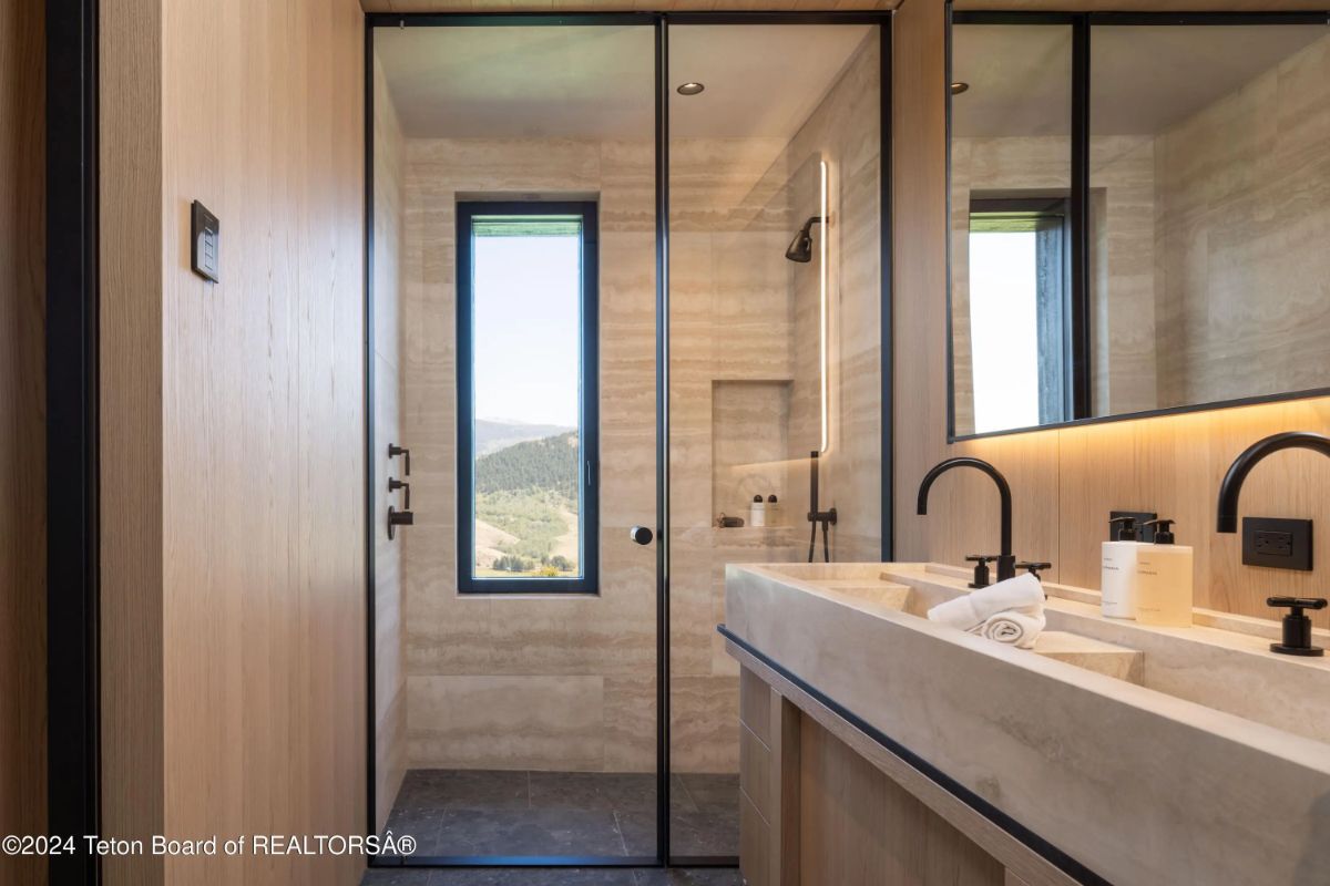 Contemporary bathroom with dual sinks, black fixtures, and a glass-enclosed shower with scenic views. 