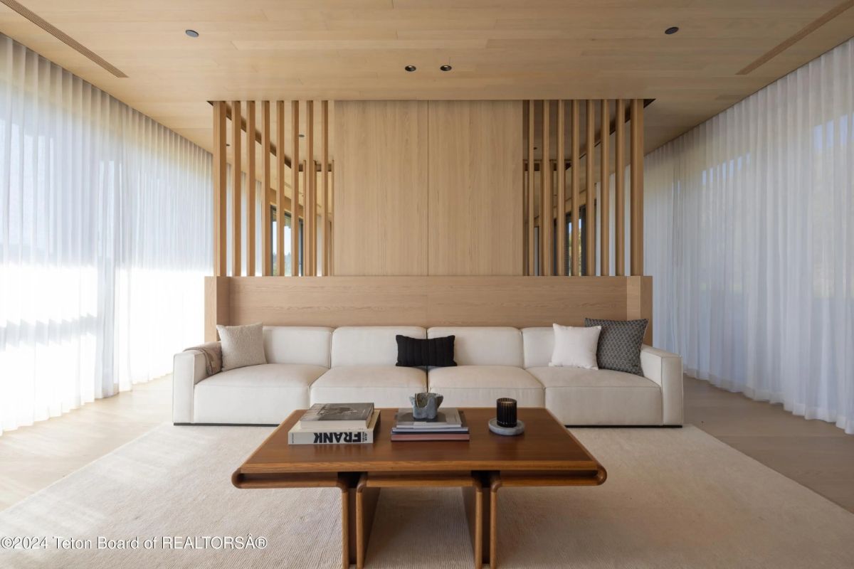 Bright and airy sitting area with a large cream sectional, wood slat accent wall, and soft natural light filtering through sheer curtains. 