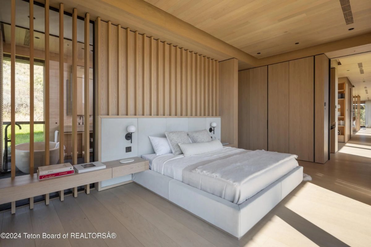 Primary bedroom featuring natural wood finishes, slatted headboard wall, and an abundance of light flowing in. 