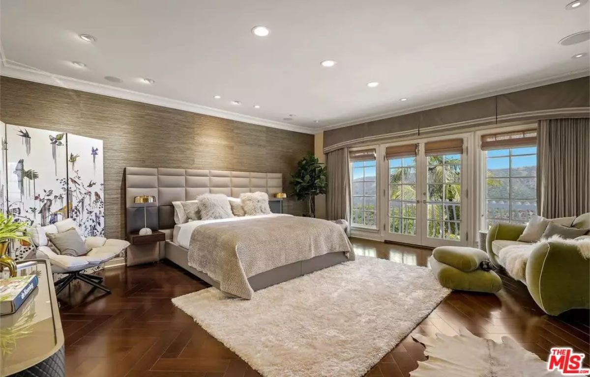 Spacious bedroom features a large upholstered headboard and neutral bedding.
