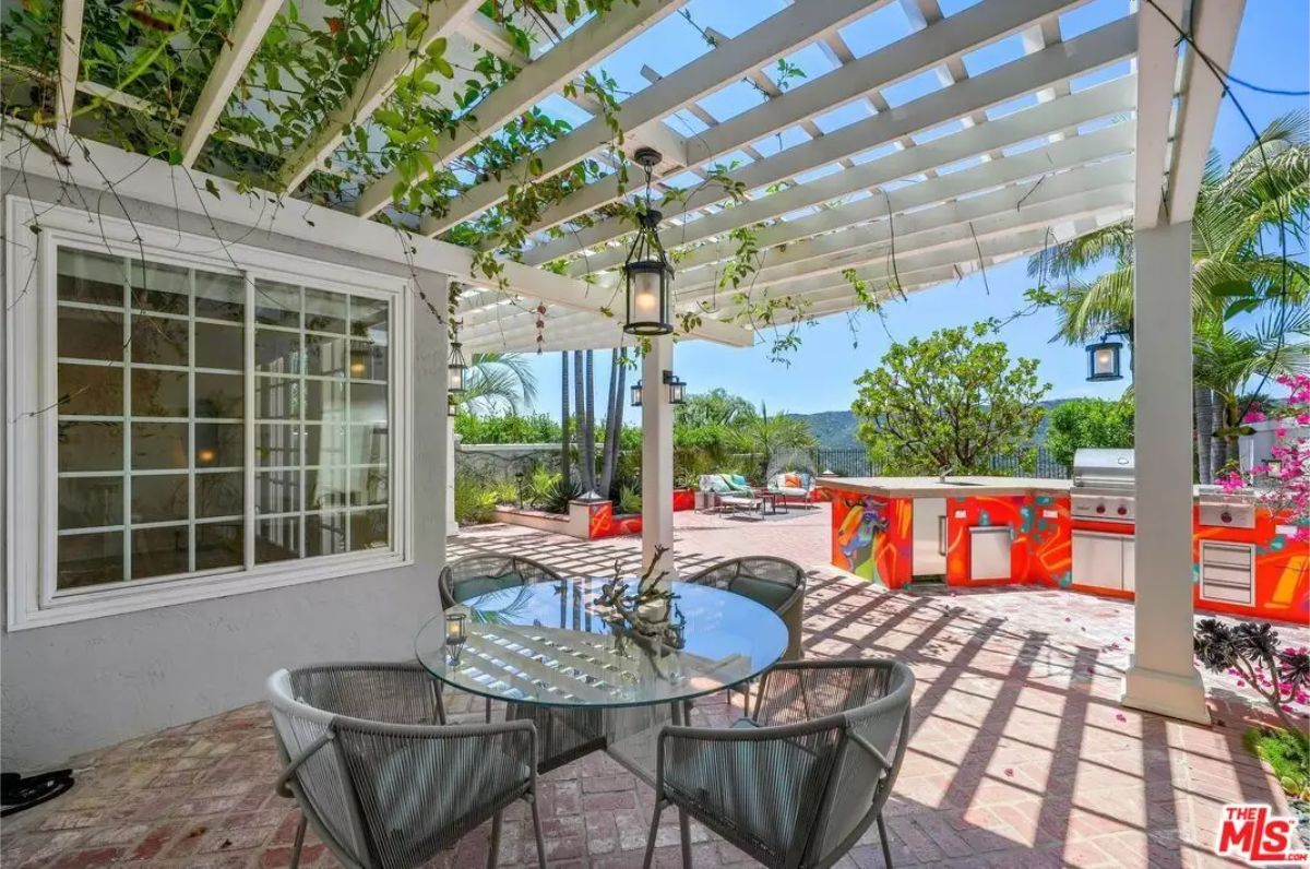 Brick patio area is shaded by a white pergola with vines.