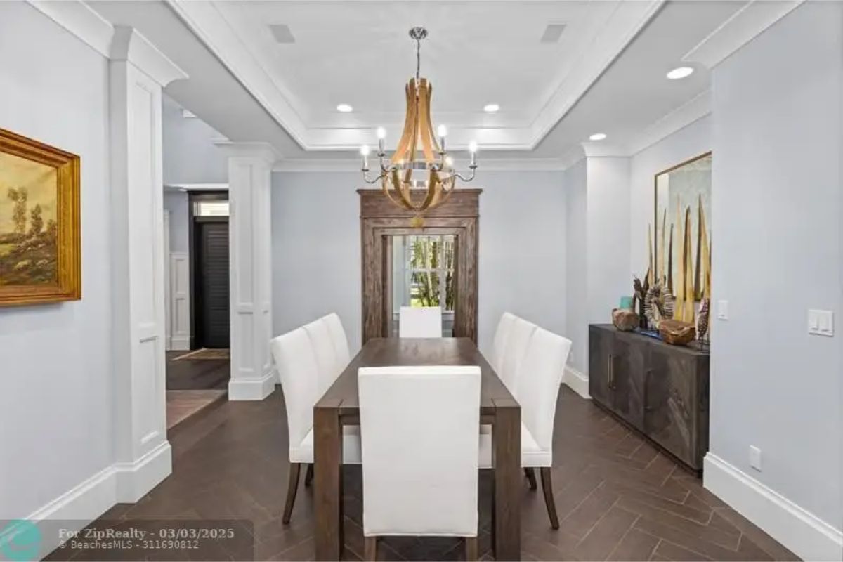 Rectangular wood table is surrounded by six white upholstered chairs.