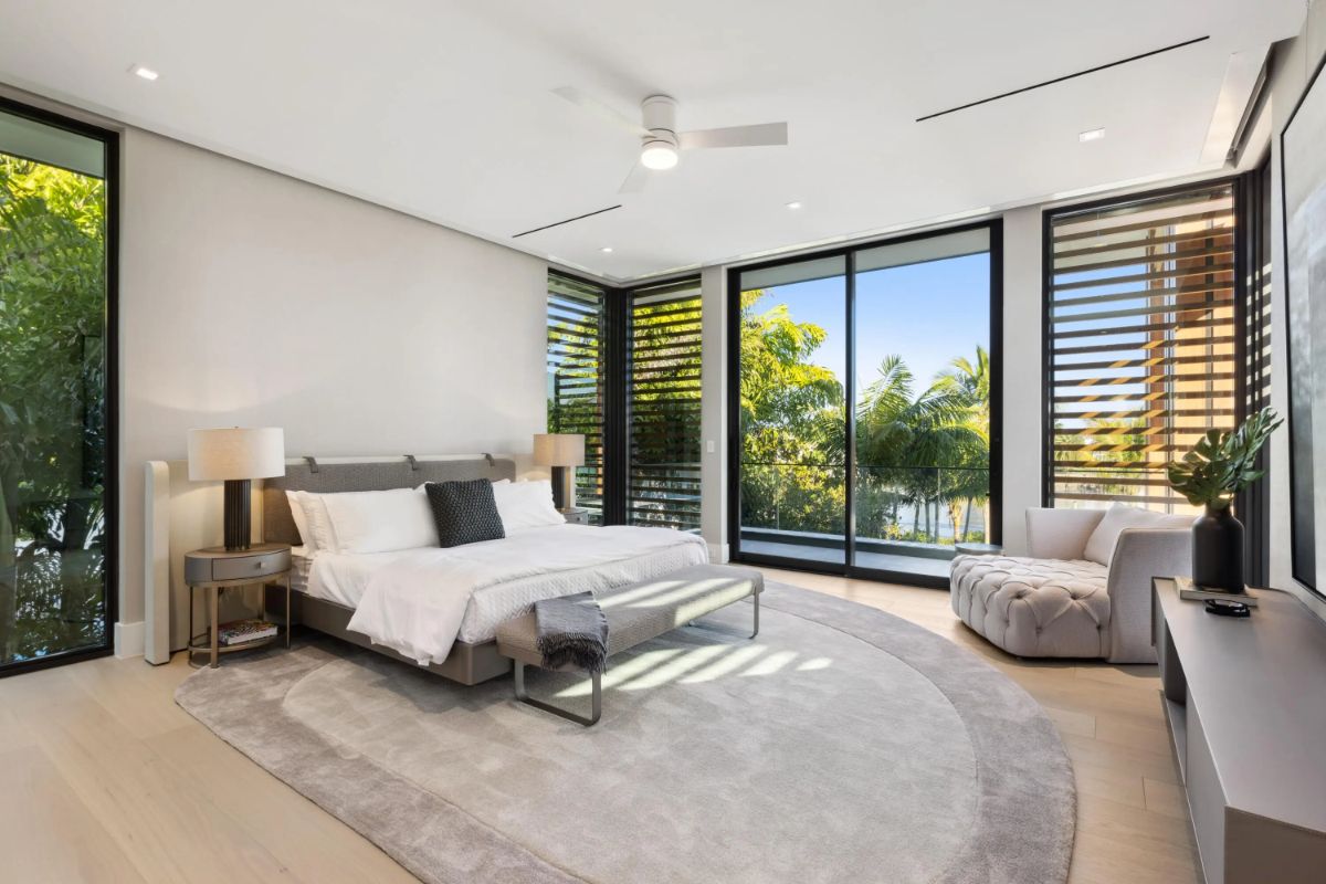 Luxurious bedroom with modern furnishings and large corner windows bringing in lush green views. 