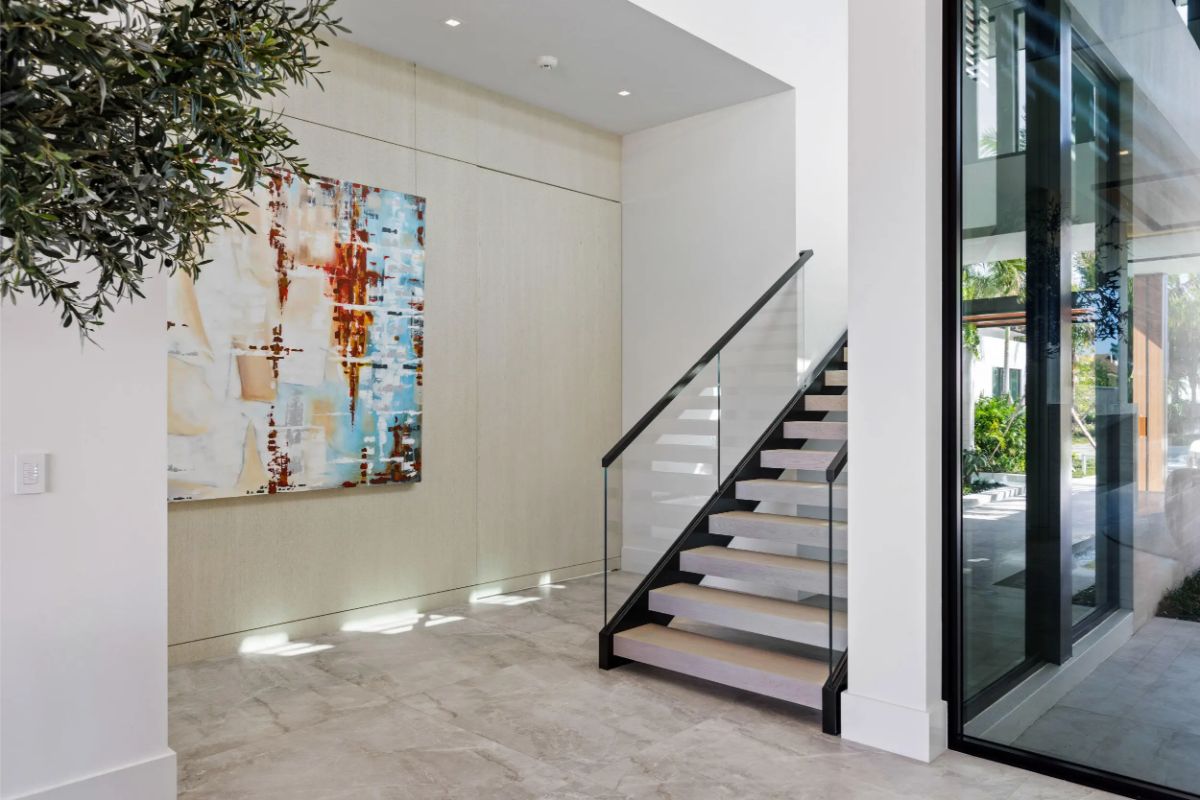 Clean-lined staircase rises beside large glass walls, adding architectural depth to the hallway. 