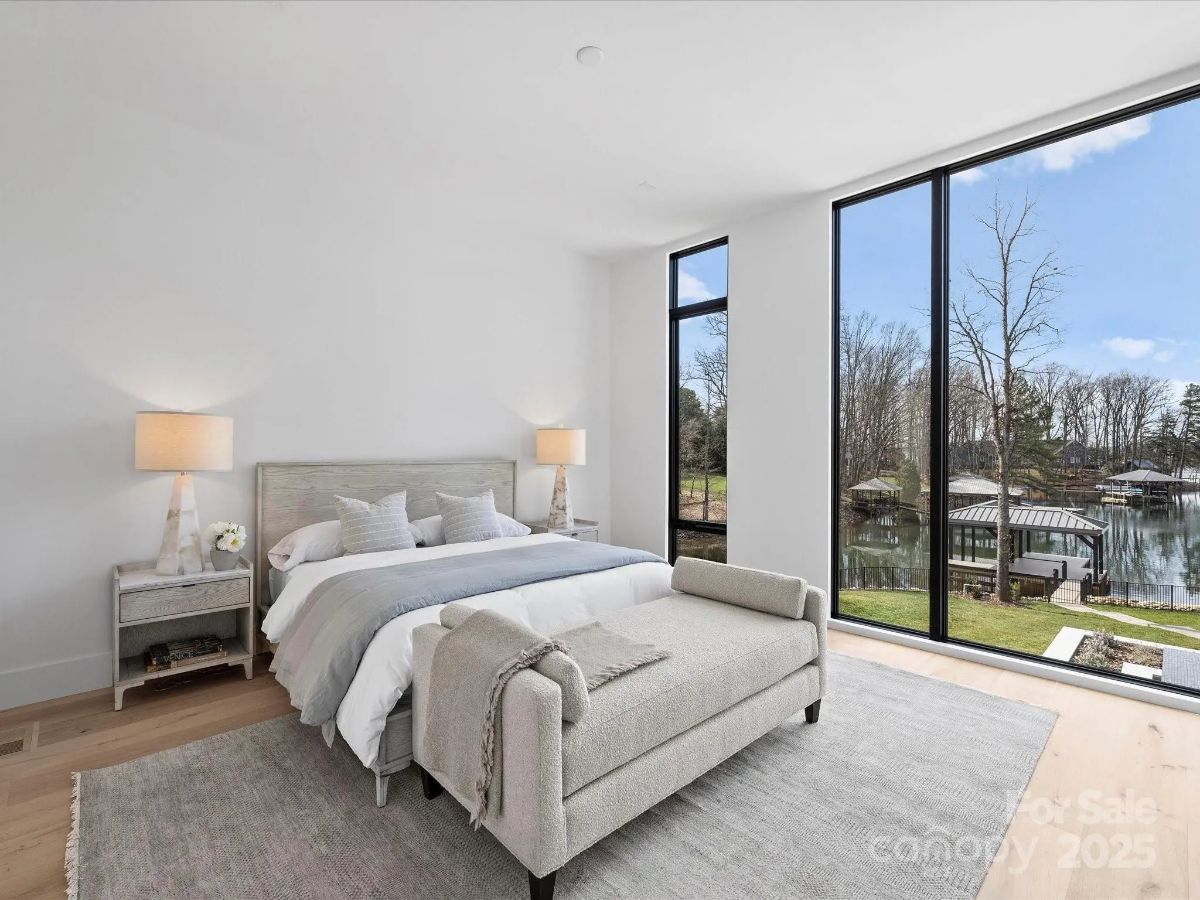 Spacious bedroom with large picture windows facing a wooded lake area.