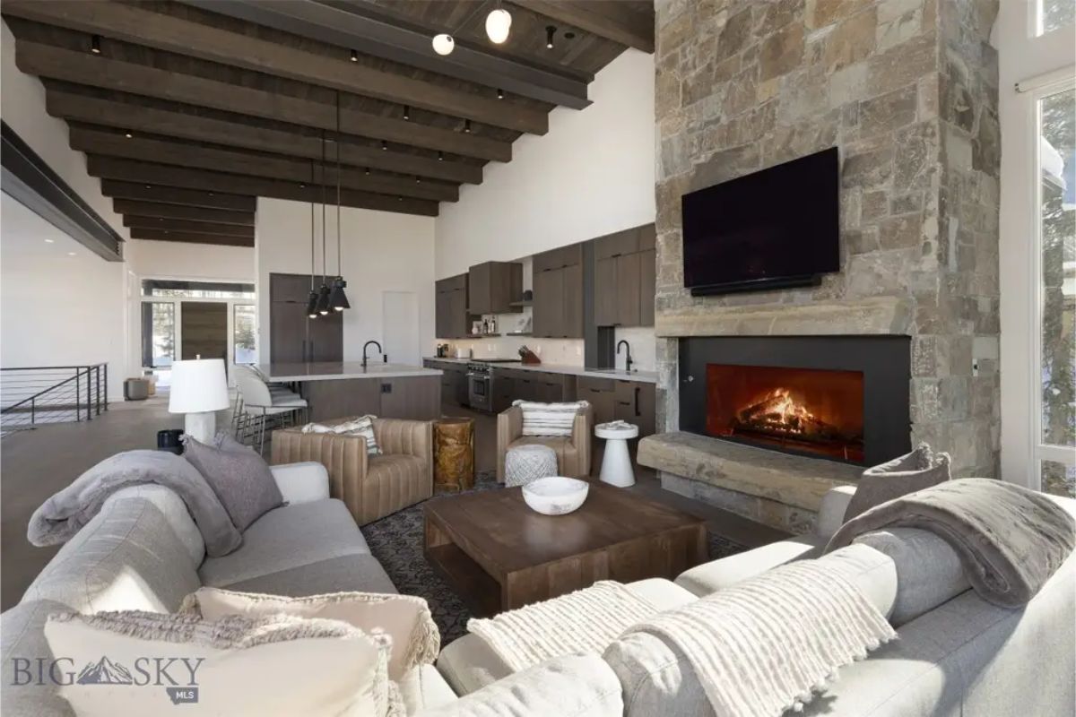 Cozy living room features a floor-to-ceiling stone fireplace, wooden ceiling beams, and plush seating for a warm ambiance.