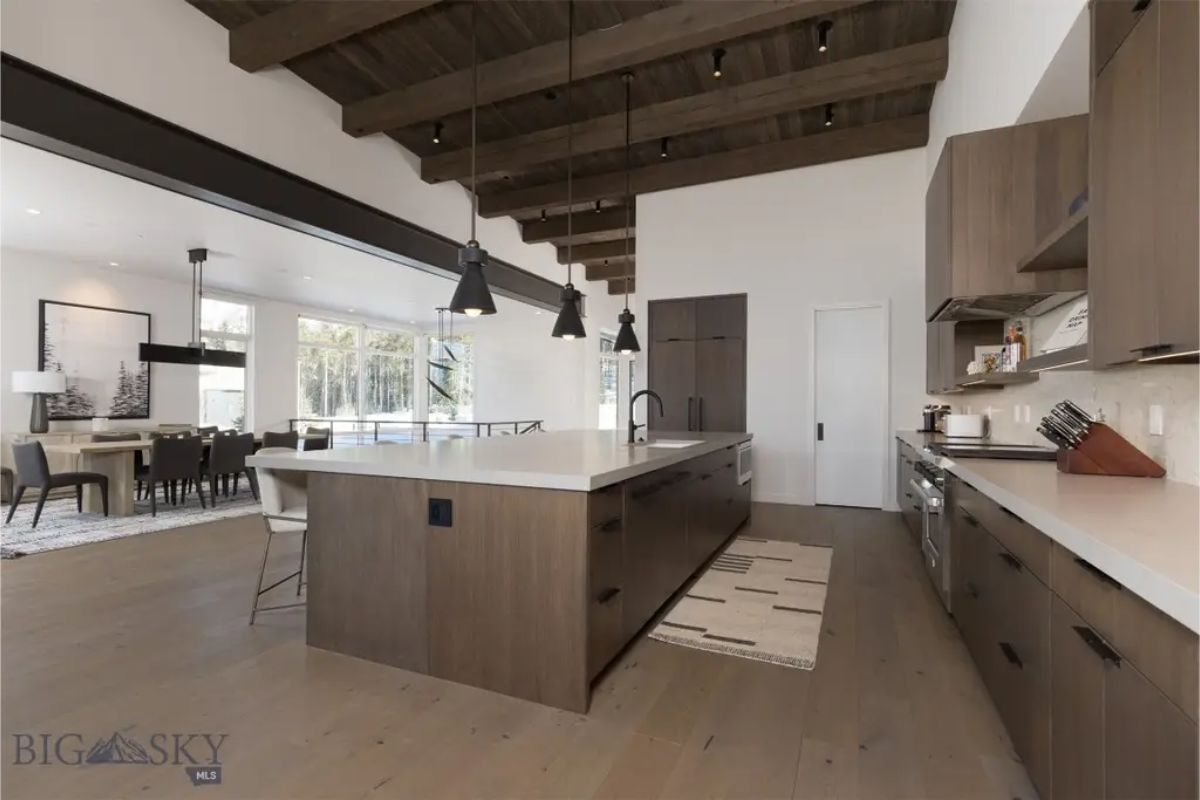 Open-concept kitchen connects seamlessly to the dining and living area, with exposed wooden beams adding a rustic touch.