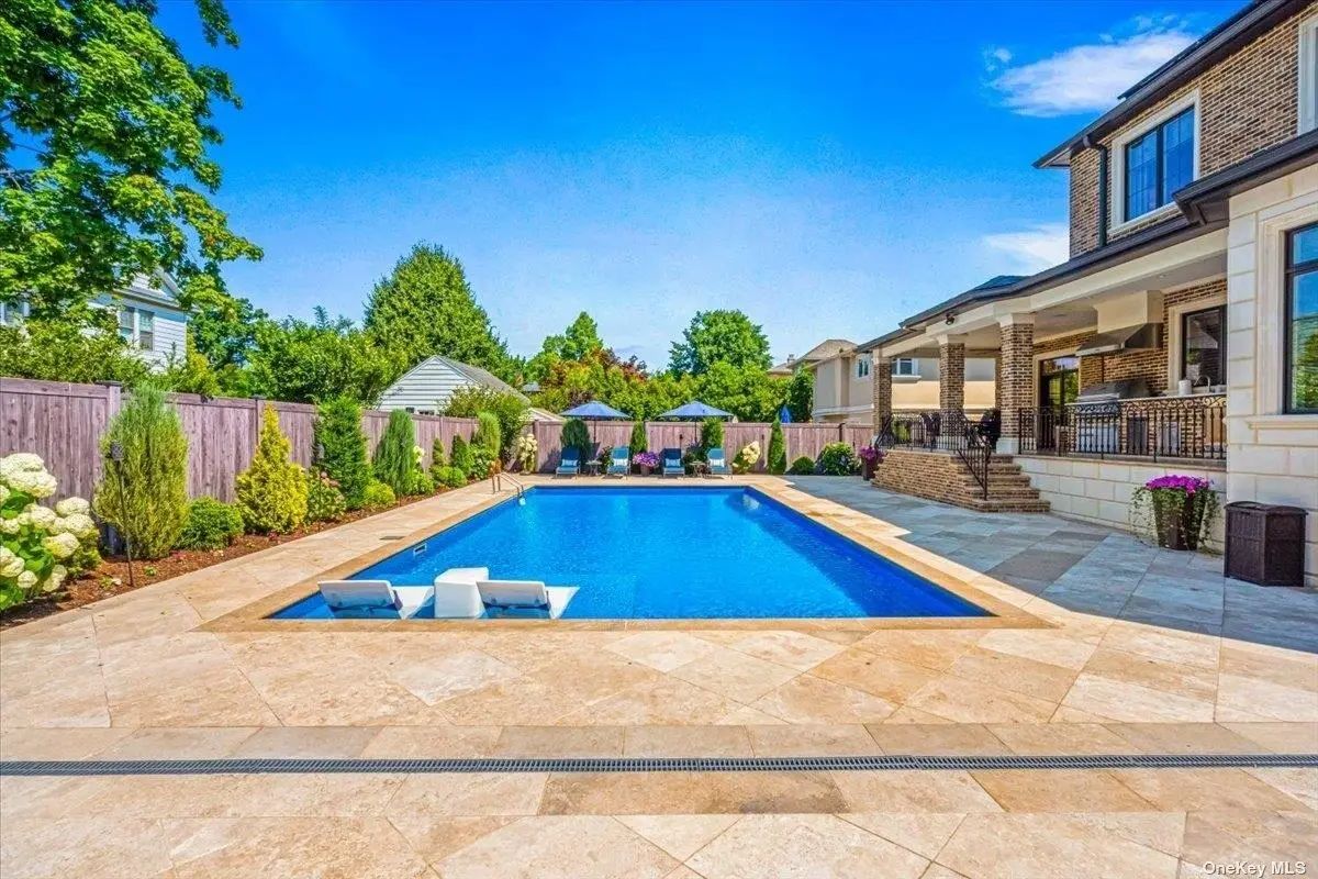 Rectangular pool is surrounded by beige tile and privacy fencing.