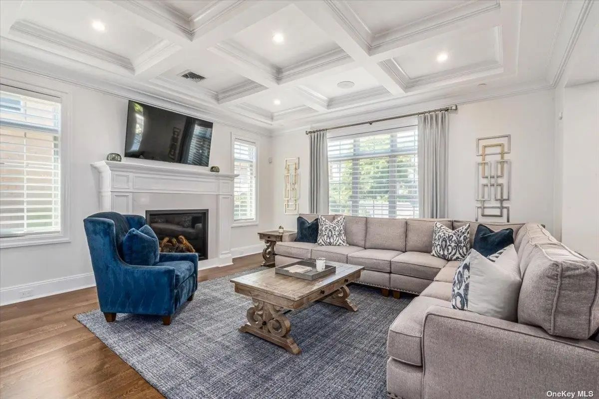 Sectional sofa and blue accent chair sit on a large navy rug facing a white fireplace.