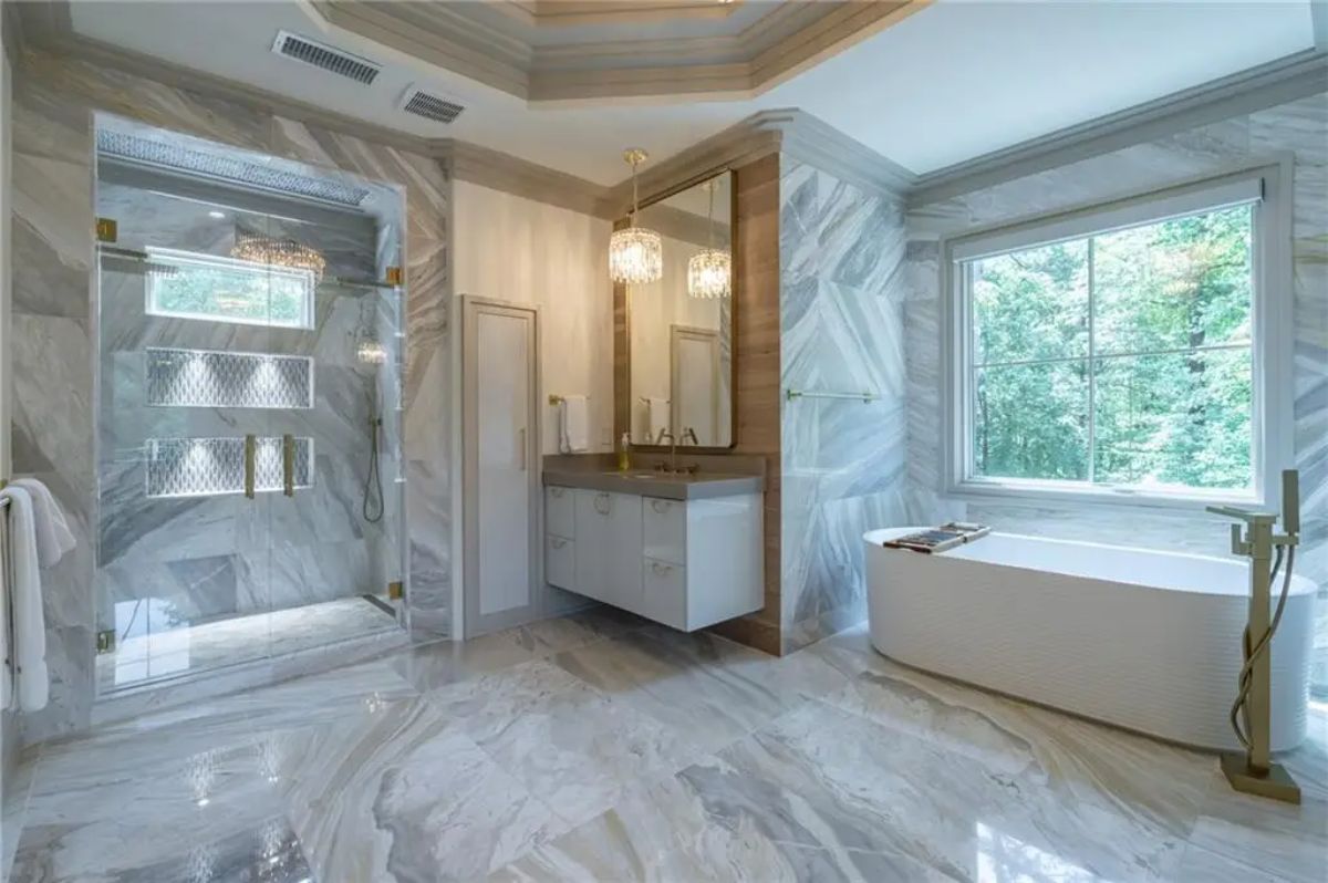 Opulent bathroom wrapped in marble with a soaking tub, walk-in shower, and gold accents. 