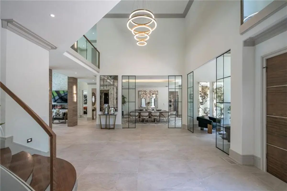 Grand entryway with soaring ceilings, modern ring chandelier, and glass-paneled double doors leading to other rooms. 