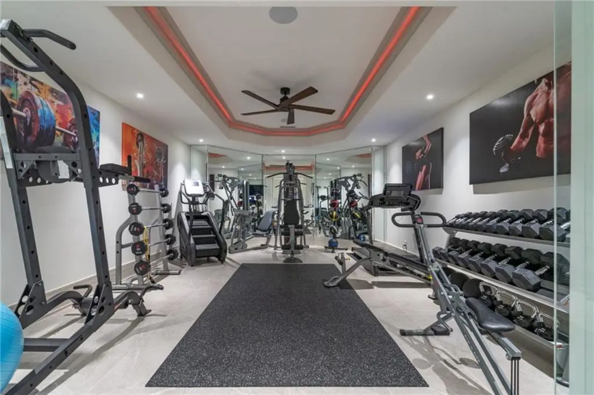 Fully equipped home gym with mirrored wall, dumbbell racks, and high-end fitness machines. 