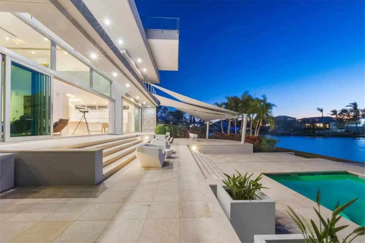 Outdoor patio at dusk with stylish seating, modern lighting, and a beautiful pool overlooking the water. 