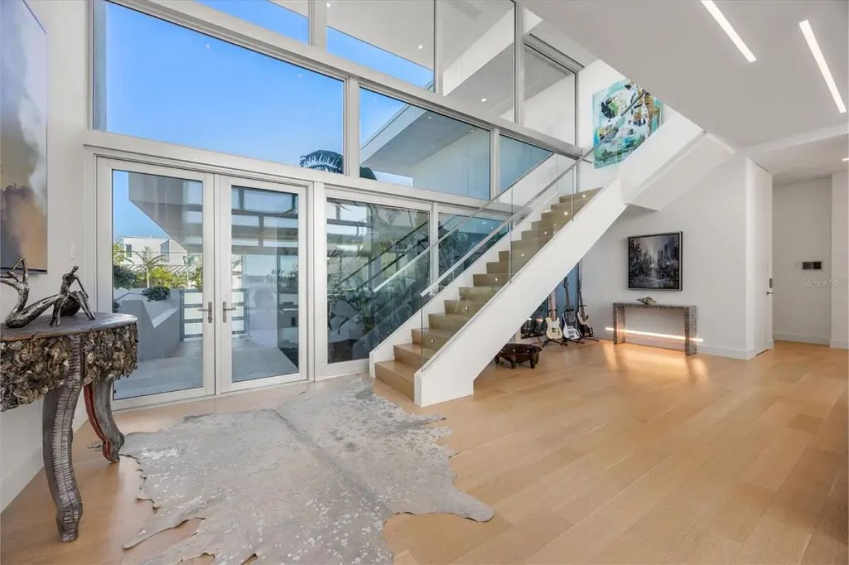 Bright and airy foyer featuring a glass staircase, modern decor, and floor-to-ceiling windows. 