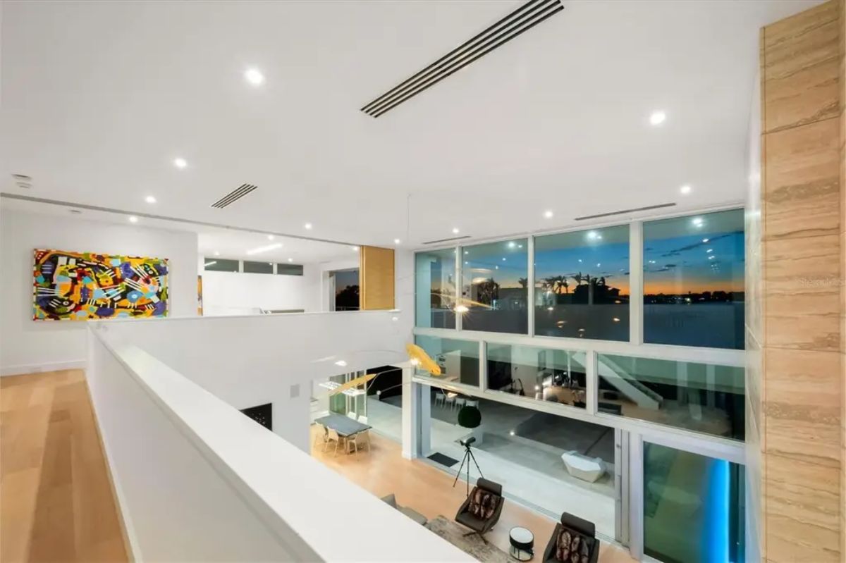Upper-level loft with a glass balcony, overlooking the main living space and the waterfront scenery. 