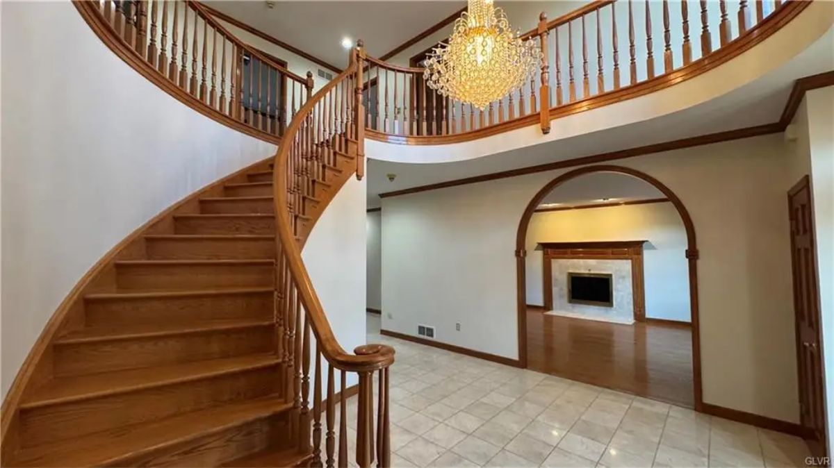 A curved wooden staircase leads to the second floor, wrapping around an open balcony overlooking the foyer.