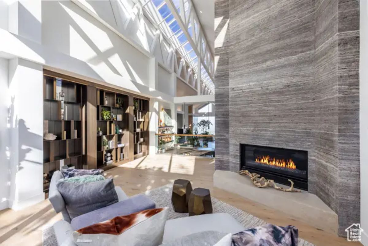 A bright living area with a high sloped ceiling, skylights, a fireplace, and an open-concept design blending into a library space. 