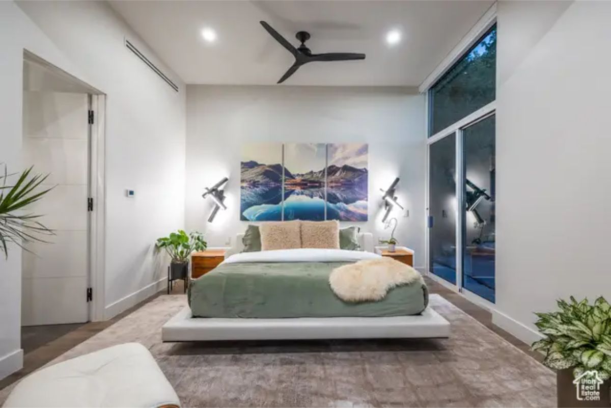 A luxurious bedroom with a modern, floating platform bed, soft green bedding, and large glass doors leading to an outdoor space. 