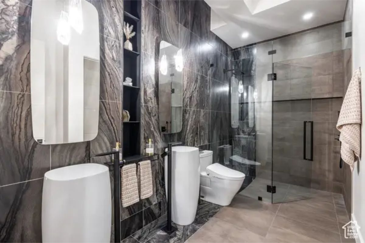 A stylish bathroom with a black and gray color scheme, featuring a glass-enclosed shower and unique pedestal sinks. 