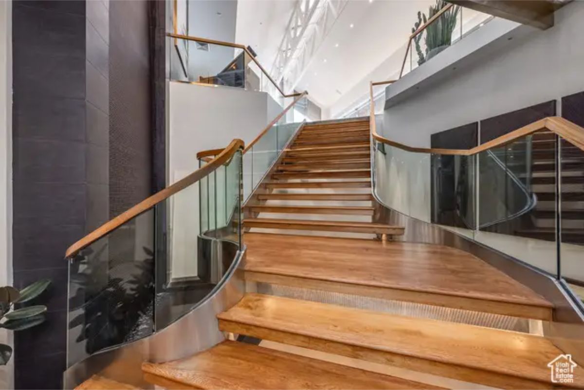 Sophisticated wooden staircase with glass railings, leading to an open second-floor area. 