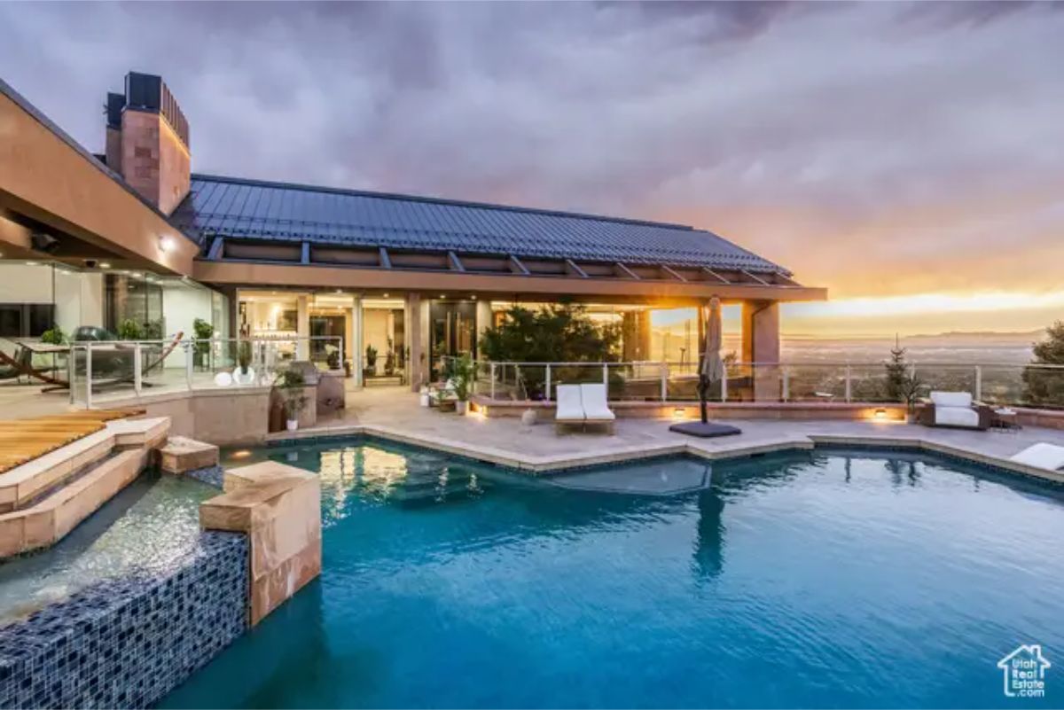 A twilight view of the house’s outdoor pool, with its glass walls reflecting the warm glow of the interior lighting. 