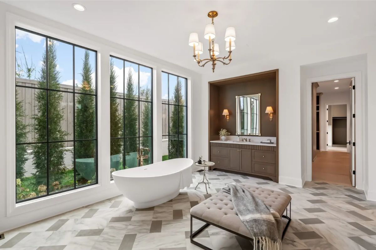 Luxurious bathroom with floor-to-ceiling windows, a freestanding tub, and elegant chandelier lighting. 