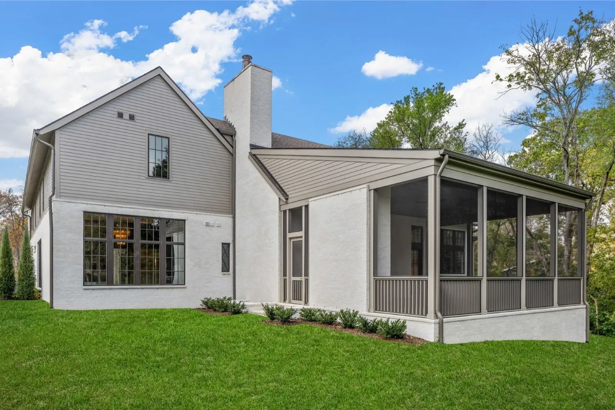 Backyard view showing a screened-in porch, neutral siding, and well-kept lawn space. 