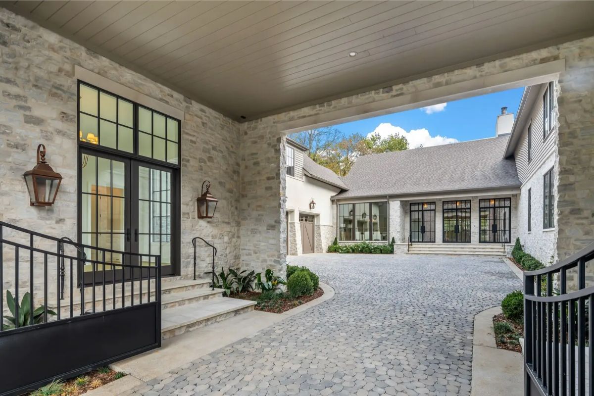 Covered motor court with cobblestone drive, black iron railings, and French doors opening into the interior. 