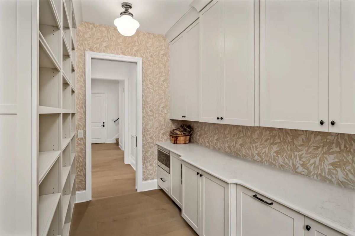 Walk-through pantry with full-height shelving, white cabinetry, and a soft floral backsplash. 