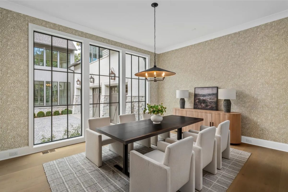 Refined dining room with a dark wood table, plush white chairs, and oversized steel windows bringing in light. 