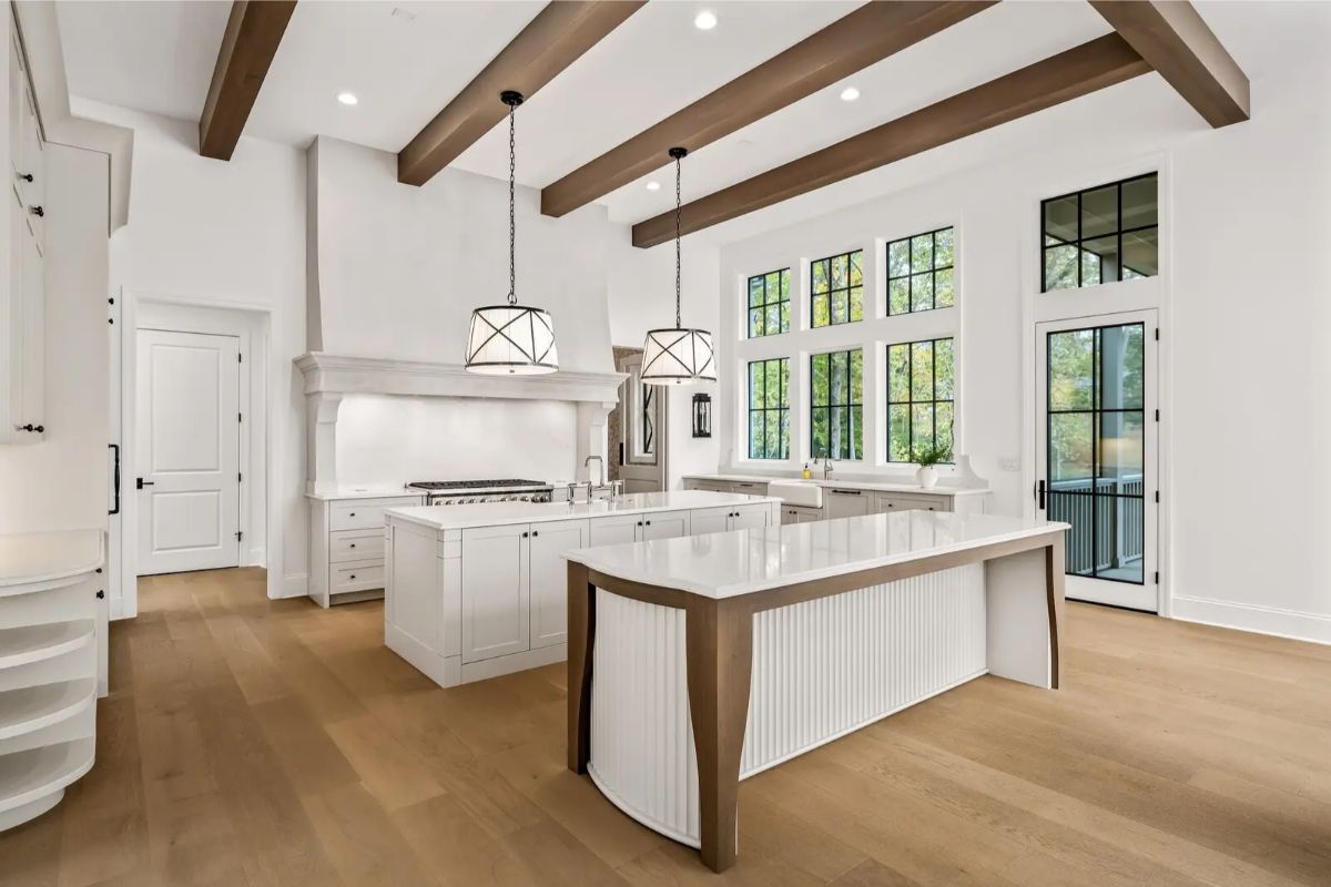 Bright white kitchen with a large center island, exposed wood beams, and statement pendant lights. 