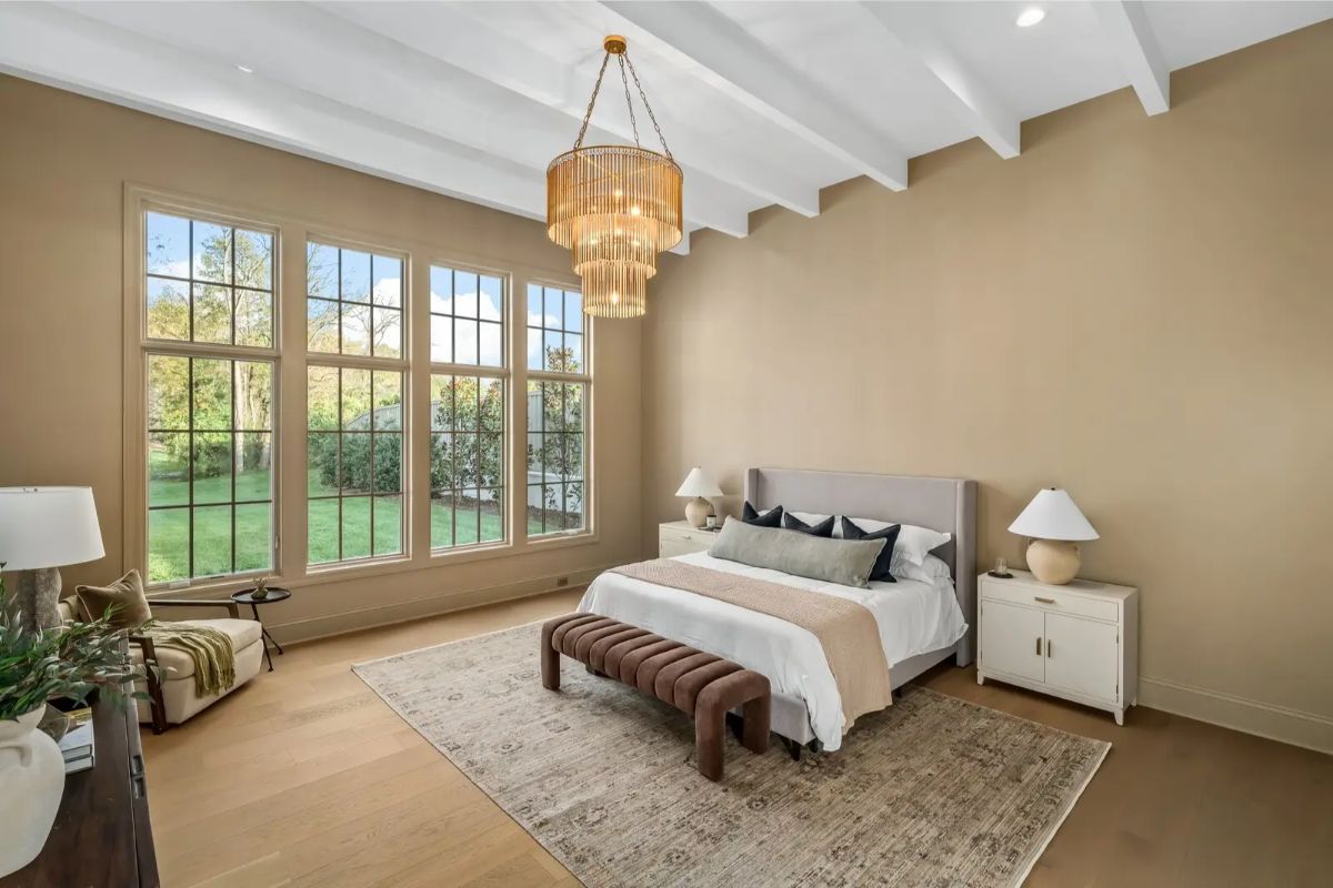 Tranquil bedroom with soaring ceilings, soft earth tones, and a large grid-style window flooding the room with light. 