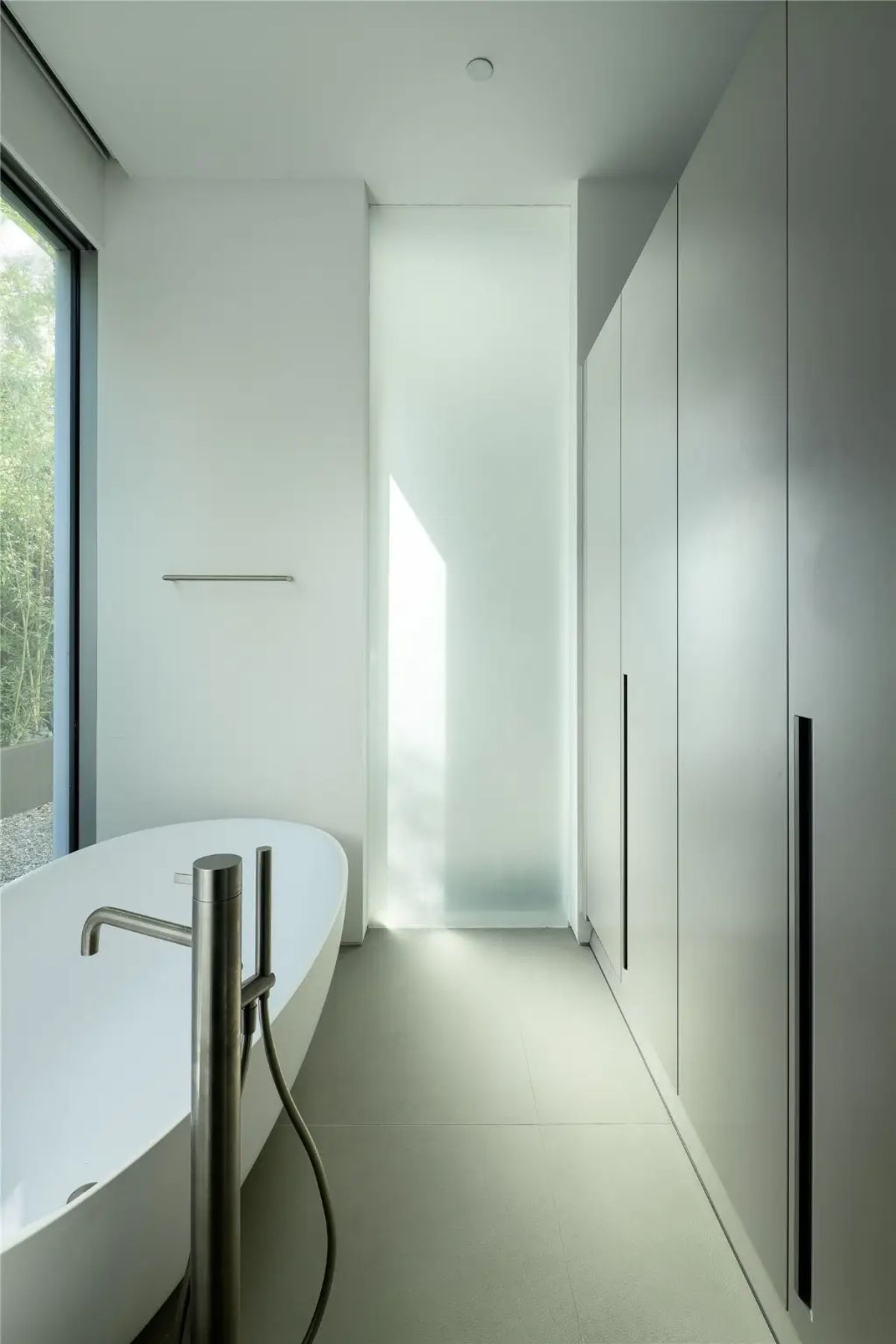 A modern bathroom with a freestanding tub, sleek cabinetry, and floor-to-ceiling frosted glass windows. 