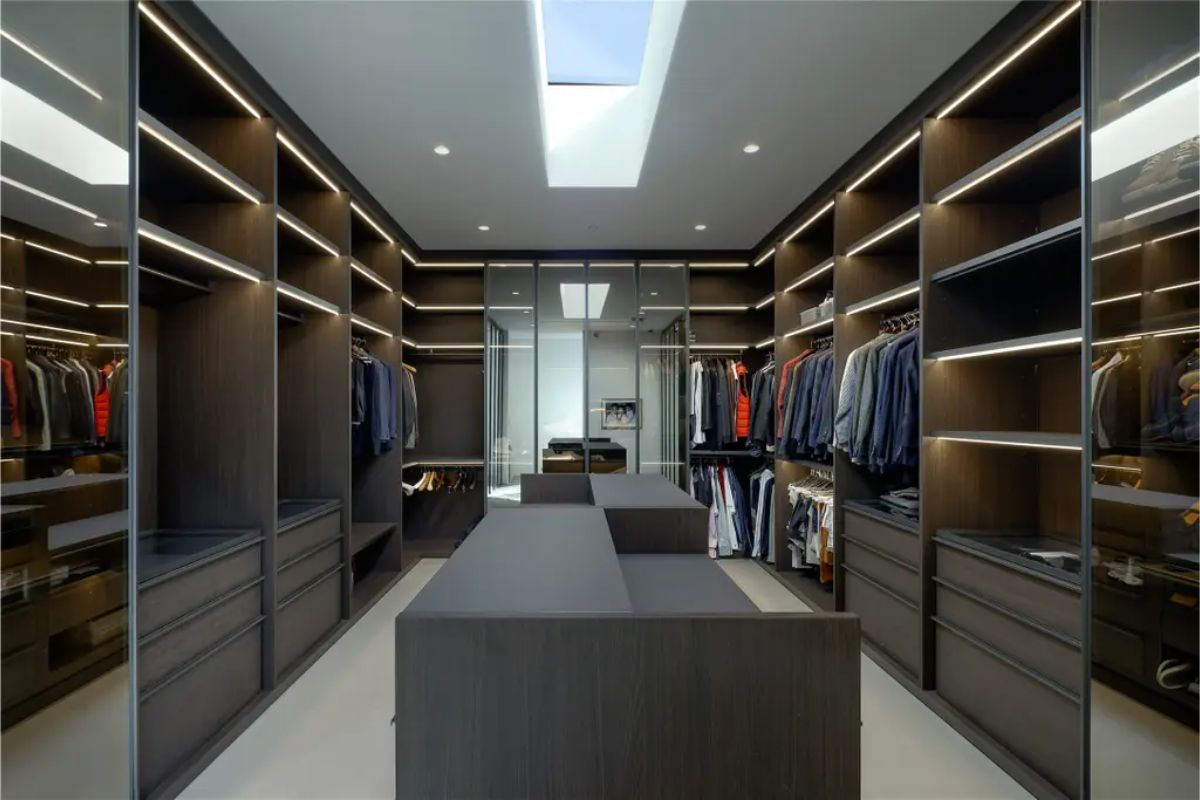 A luxurious walk-in closet with dark wood shelving, recessed lighting, and a skylight. 