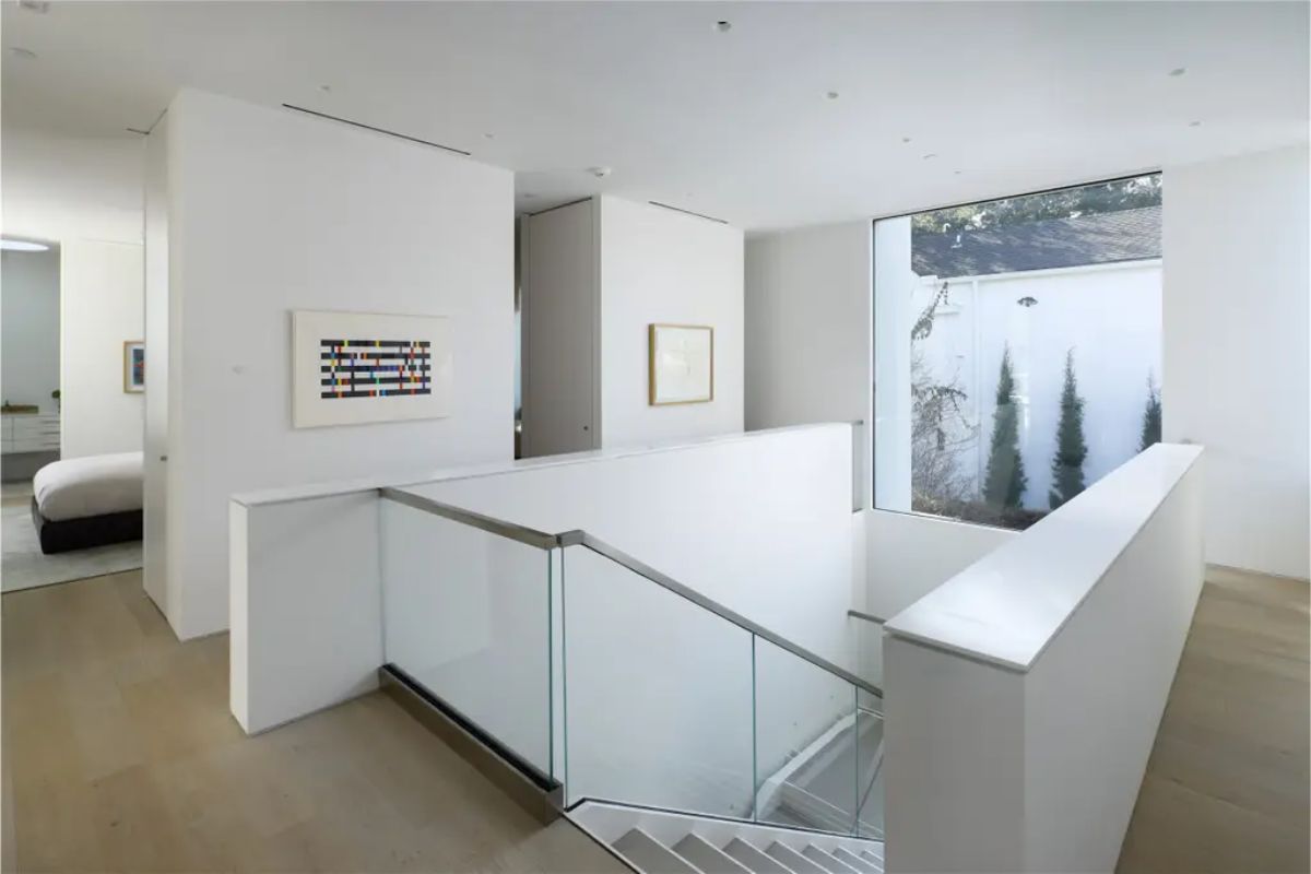 Bright and modern upper landing with glass railings and a view of the outdoor greenery. 
