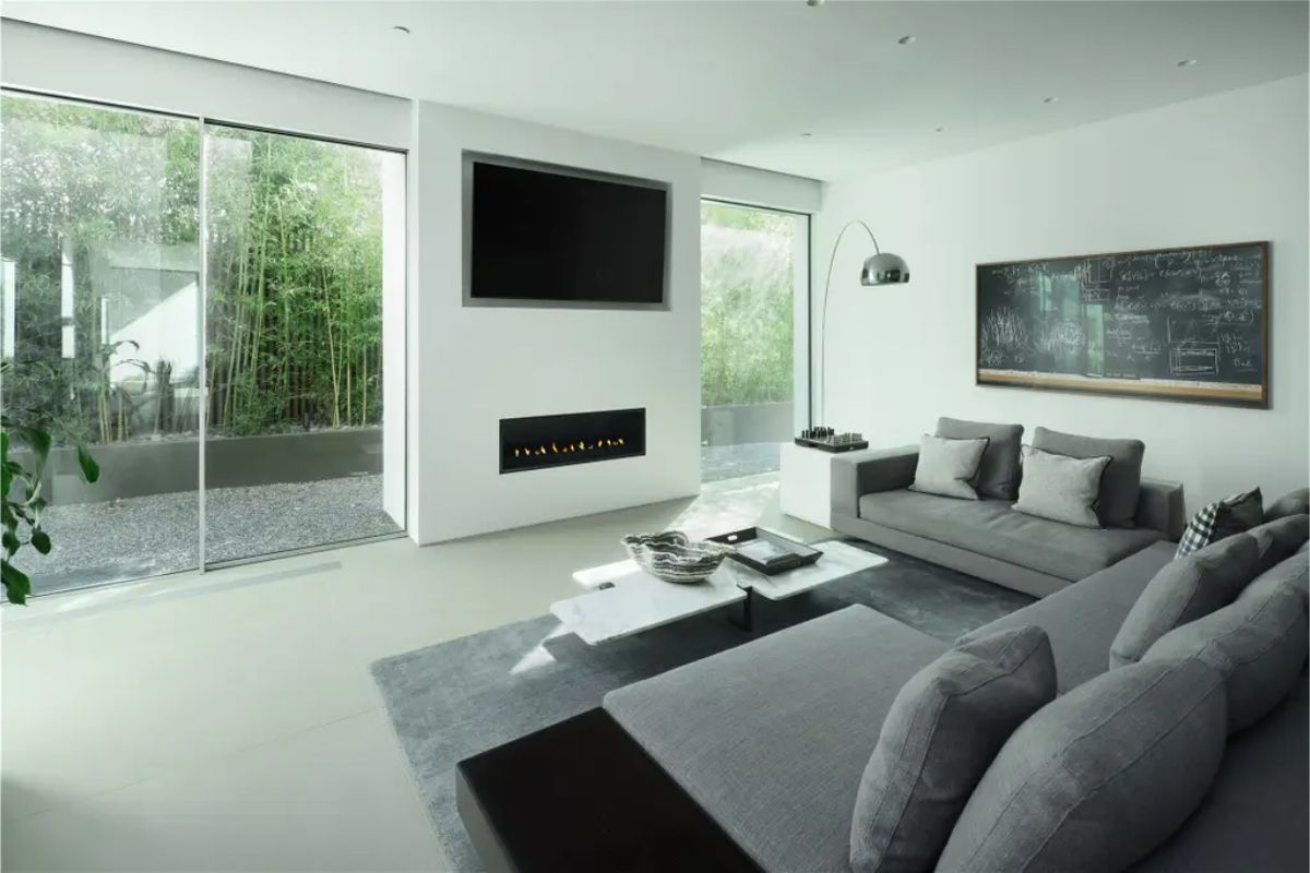 Cozy living space with a neutral palette, built-in fireplace, and floor-to-ceiling windows leading to a private garden. 
